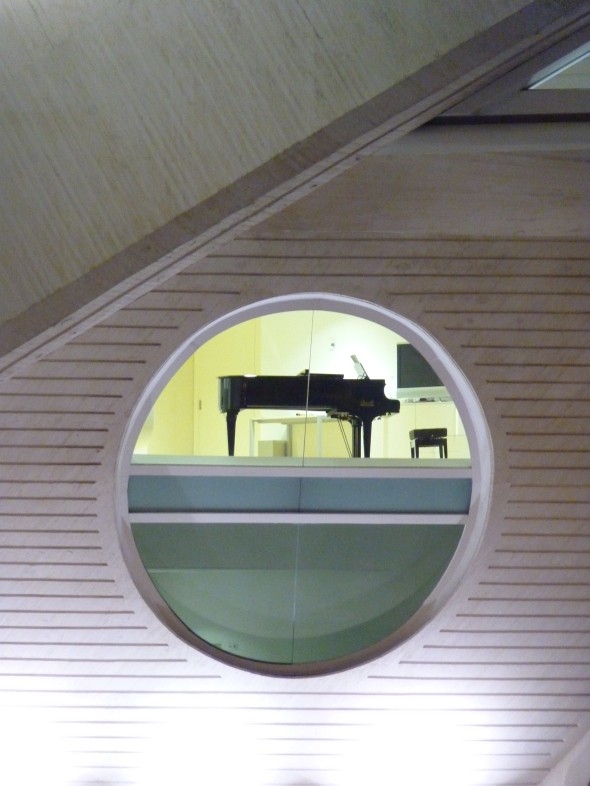 piano à queue derrière une vitre en forme de hublot